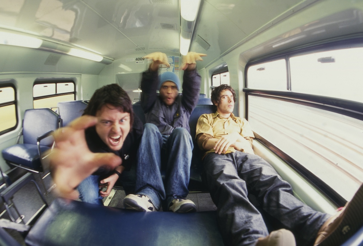 Candid wide-angle shot of Australian band Gerling fooling around inside a train carriage, sitting on blue seats.